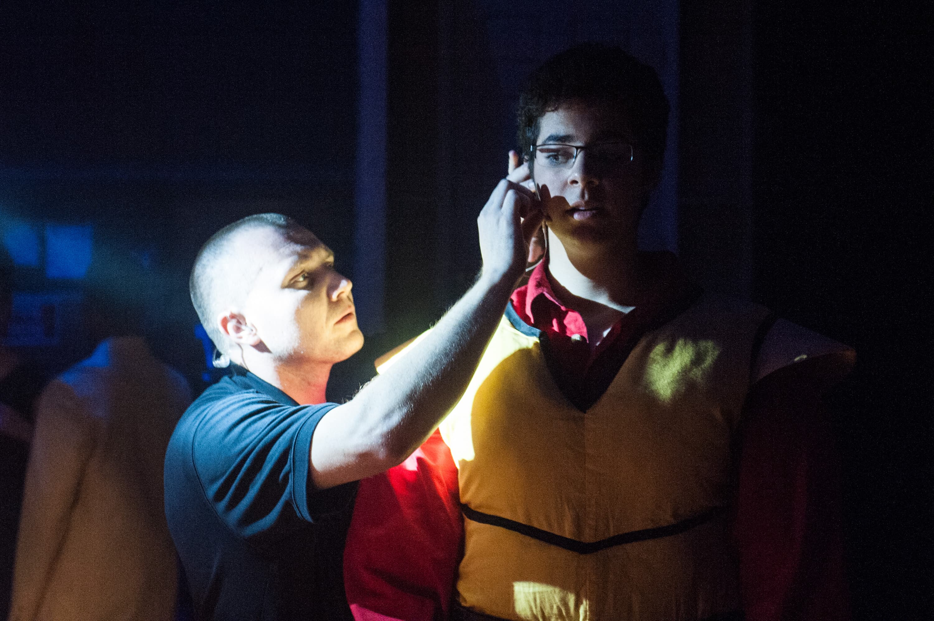 A person is adjusting the microphone on another person who is wearing a yellow vest.