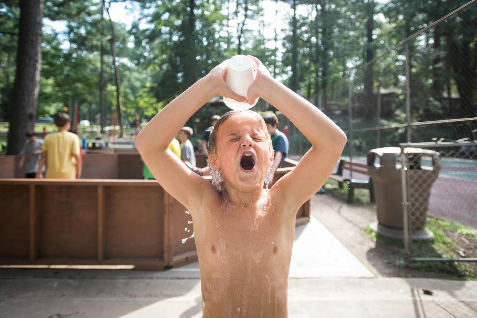 Boy dumping a cup of water over his head at a summer camp to cool off.