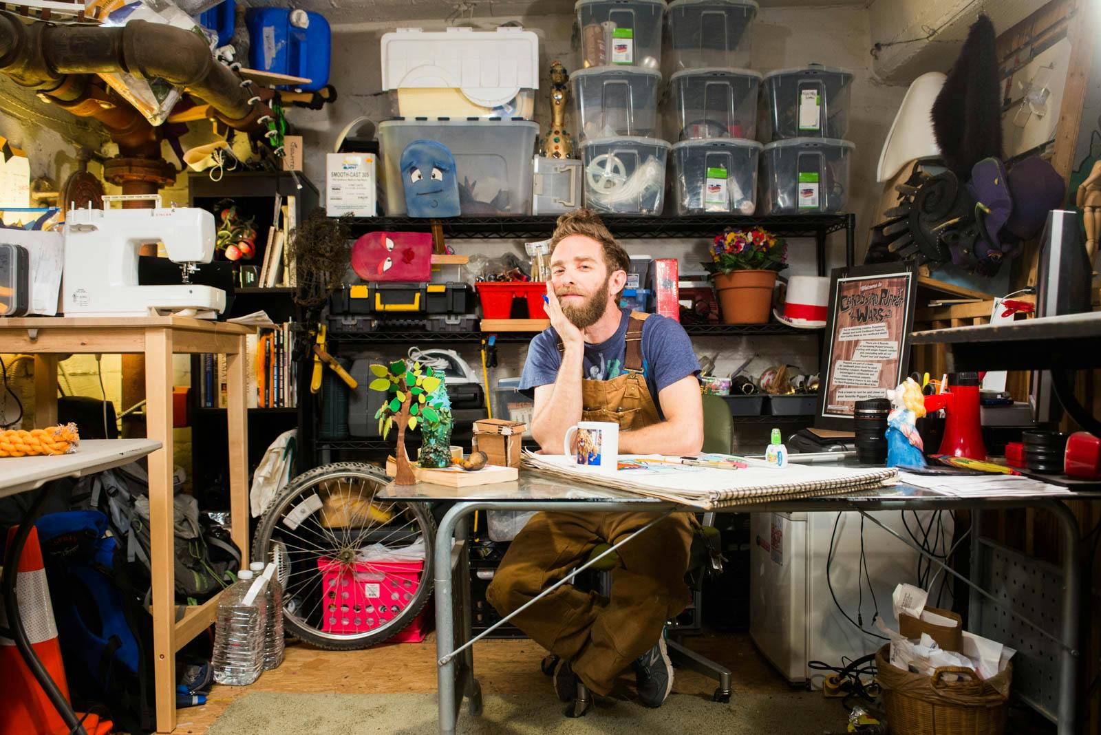 A puppeteer at a desk in his workshop, looking at the camera.