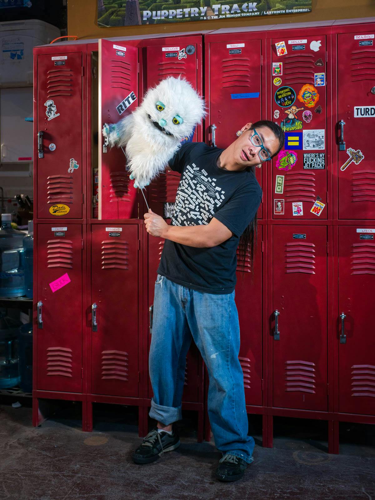 A puppeteer standing in front of red lockers, holding a puppet.