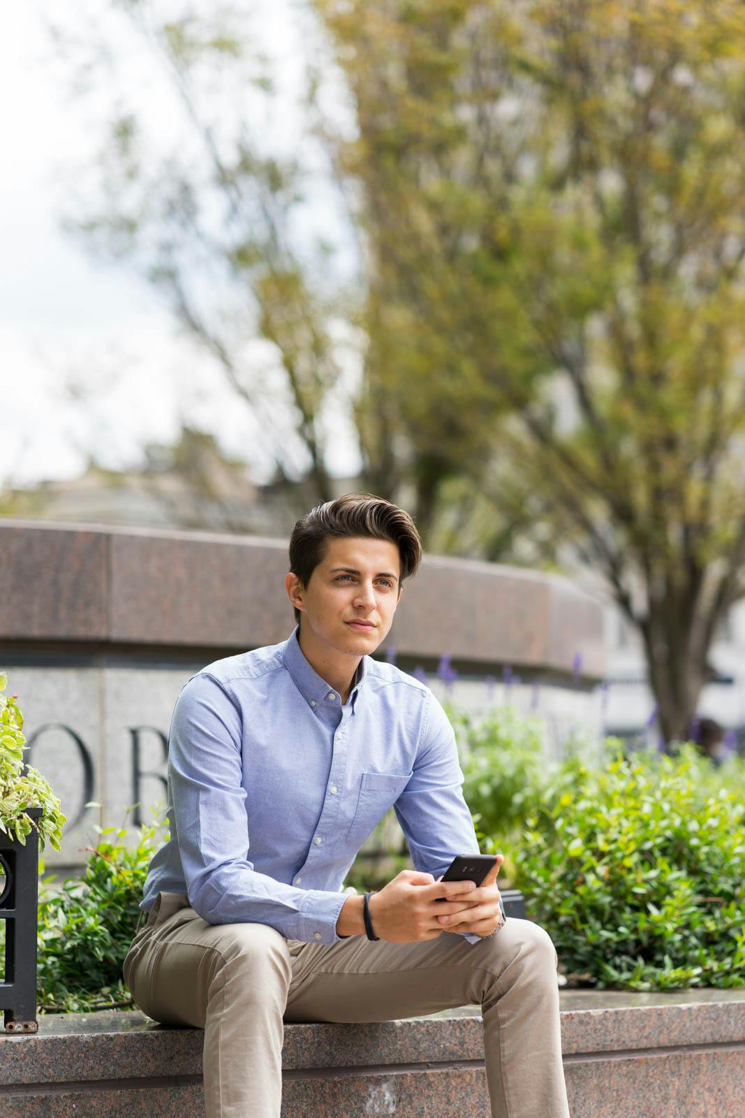 A young man holding his phone and sitting on a low wall in Woodruff Park, Atlanta, GA.